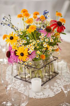 a vase filled with lots of colorful flowers on top of a table next to wine glasses