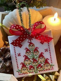 a cross stitch ornament hanging from a christmas tree with candles in the background