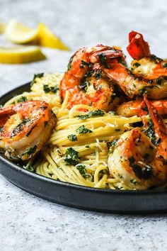 some shrimp and pasta on a plate with lemon wedges in the backround