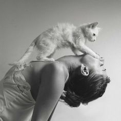 a black and white photo of a woman holding a cat on her shoulders