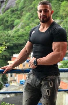 a man in black shirt standing on top of a metal rail next to trees and buildings