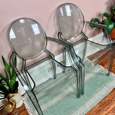 three clear glass chairs sitting on top of a wooden floor next to a potted plant