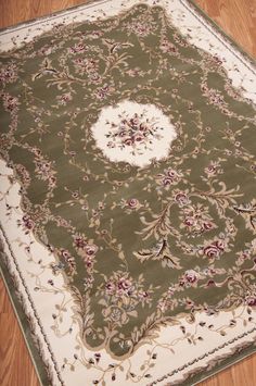 a green rug with white border and floral design on the center is laying on a wooden floor