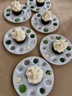 four cupcakes are sitting on plates with white frosting and green sprinkles