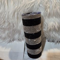 a black and white striped tumbler with silver sequins on the side sitting next to a fluffy white pillow