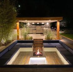 a fire pit in the middle of a patio with seating around it at night time