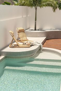 a chair and umbrella sitting on the edge of a pool next to a palm tree