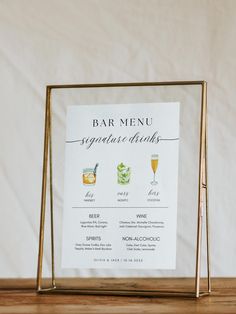 a bar menu is displayed on a wooden table with white linens and gold frame