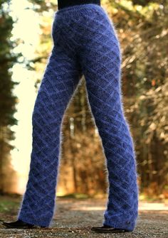 a woman wearing blue knitted pants and black shoes standing in front of some trees