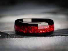 Say 'I do' in style with this awesome black and red wedding band! The 8mm band is as strong as your commitment, while the vibrant lab-grown garnet inlay adds a fiery, fun twist to your love story. It's not just a ring; it's a statement, a symbol of your unique love, and a conversation starter. Slip it on, own the moment, and let your personality shine bright. This tungsten ring features a polished black color, and an inlay of lab grown garnet gemstone. - High-quality tungsten carbide - Black pol Garnet Rings For Men, Formal Black Rings With Ruby, Round Black Ruby Ring, Black Round Ruby Ring, Black Ruby Ring For Anniversary, Black Ruby Anniversary Ring, Black Ruby Wedding Jewelry, Black Ruby Jewelry For Wedding, Wedding Black Ruby Jewelry