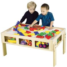 two young boys playing with toys in a play table on a white background, one boy is looking at the toy