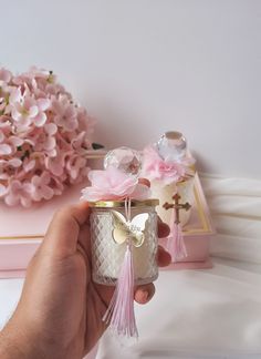 a hand holding a small glass jar with pink flowers in it and a cross on the top