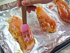 a hand holding a brush over some food on tin foil with other foods in the background