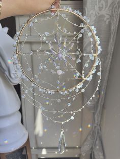 a person holding a gold and white dream catcher with crystals on it's sides