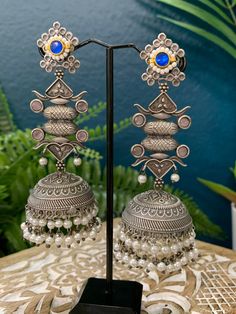 This silver replica statement jhumki earring is crafted with exquisite detail and superior quality. With a combination of kemp stone, kundan work, and pearl drop, these lightweight earrings are sure to be a stylish statement piece. About 4.5inch long and 1.5 inch wide Silver Kundan Chandbali Jhumkas, Silver Kundan Jhumkas With Intricate Design, Temple Jewelry Kundan Earrings With Oxidized Finish, Traditional Chandbali Jhumkas For Designer Wear, Bohemian Silver Earrings With Stone Work, Silver Kundan Jhumkas With Tilla, Silver Kundan Chandelier Earrings With Tilla, Silver Kundan Chandelier Earrings With Meenakari, Silver Meenakari Kundan Chandelier Earrings