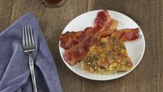 two pieces of bacon on a plate next to a fork and cup with tea in it