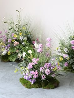 three vases filled with flowers sitting on top of a cement floor covered in grass