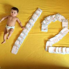 a baby laying on top of a yellow blanket next to two diapers that are shaped like numbers