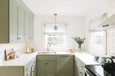 a kitchen with green cabinets and white counter tops, along with a window over the sink