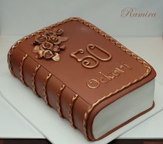 a book shaped cake on top of a white plate with gold trimmings and flowers