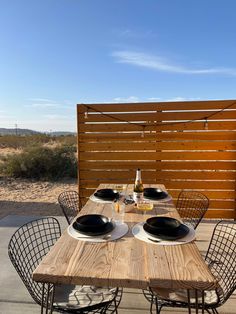 a wooden table topped with black plates sitting next to a wooden fence covered in wood slats