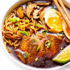 a bowl filled with noodles, meat and veggies next to chopsticks