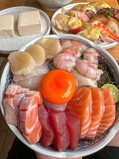 a person is holding a bowl full of different types of sushi and sashimi