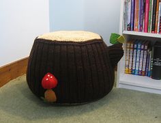 a knitted teapot with a mushroom on it in front of a bookshelf