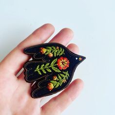 a hand holding a small embroidered bird brooch