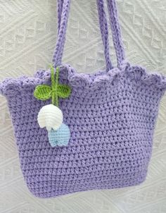 a purple crocheted bag with a flower on the side hanging from a hook