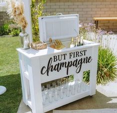 a white box with champagne on it sitting in the middle of a yard next to some flowers