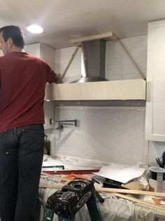 a man standing in a kitchen next to a stove top oven under construction with tools on the floor