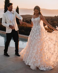 a bride and groom hold hands as the sun goes down on their wedding day in front of an outdoor swimming pool