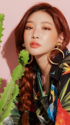 a woman with long red hair wearing large gold hoop earrings sitting next to a plant