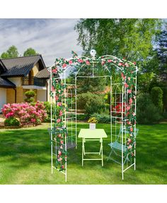 a white metal gazebo with flowers on it and a table in the grass next to it