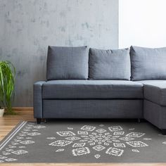 a gray couch sitting on top of a wooden floor next to a rug and potted plant