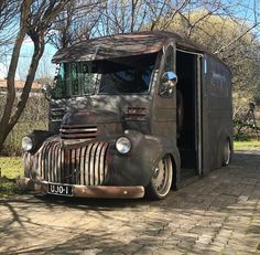 an old, rusty truck is parked on the side of a brick road in front of some trees