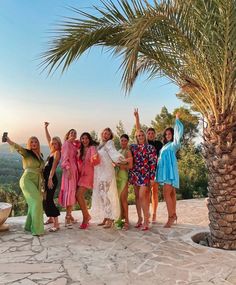 a group of women standing next to each other under a palm tree on top of a hill