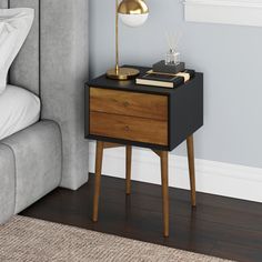 a bedside table with a lamp on it next to a bed