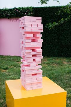 a stack of pink blocks sitting on top of a yellow box in front of a hedge