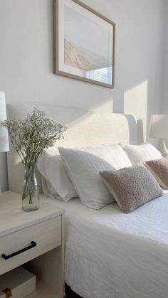 a bed with white sheets and pillows next to a vase filled with baby's breath flowers