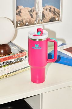 a pink coffee mug sitting on top of a white desk next to books and magazines