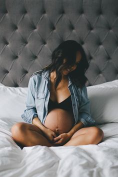 a pregnant woman sitting on a bed with her belly tucked under her stomach and looking down