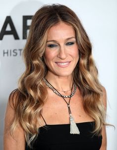 a woman with long, wavy hair wearing a black dress and smiling at the camera