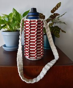 a red and white crocheted water bottle cover sitting on top of a wooden table