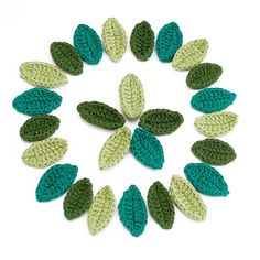 crocheted leaves arranged in a circle on a white surface with green and blue colors