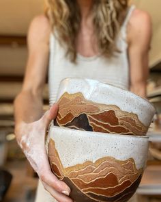 a woman holding two bowls in her hands with mountains painted on the inside of them