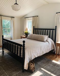 a bedroom with a bed, nightstand and windows in the room that has white curtains