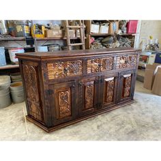 an old wooden cabinet with carvings on the doors and drawers in a workshop area, surrounded by other tools