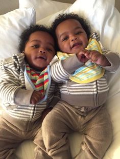 two small children laying on top of a bed next to each other, one is holding his arm around the other